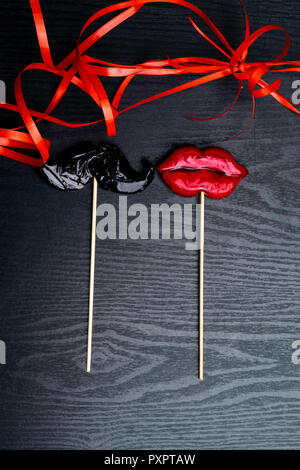 Close up de moustache et femelle, rouge lèvres bonbons, décoré de ruban rouge sur fond de bois noir, le désherbage et l'amour concept Banque D'Images