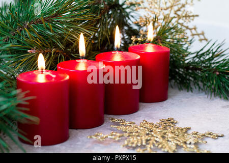 Quatre bougies de l'avent en feu rouge et une branche de sapin sur fond clair Banque D'Images