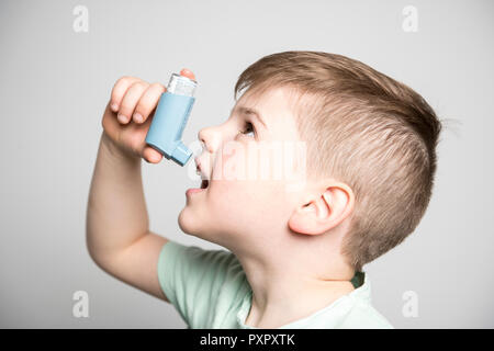 Petit garçon en utilisant sa pompe d'asthme sur studio fond blanc Banque D'Images