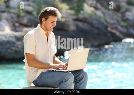 Heureux guy utilise un ordinateur portable E-mail écrit en vacances sur la plage Banque D'Images