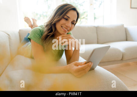 Smiling mature woman lying on couch à domicile à l'aide de tablet Banque D'Images