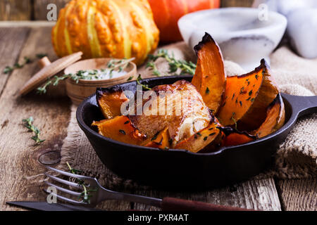 Cuisses de poulet rôti avec des tranches de courge Butternut pumpkin et thym frais dans la poêle en fonte sur table en bois rustique, automne ou hiver dîner confortable Banque D'Images