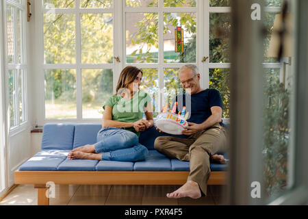 Mature Woman sitting on sofa at home with fake birthday cake Banque D'Images