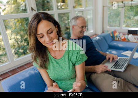 Young couple sitting on sofa at home with woman and man using laptop Banque D'Images