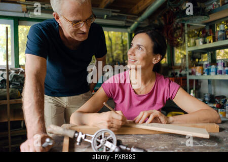 Smiling mature man watching woman working in workshop Banque D'Images