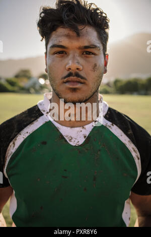 Young sportsman looking at camera en se tenant sur le sol. Close up portrait of young rugby player traînées dans la boue. Banque D'Images
