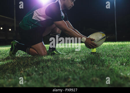 joueur de rugby plaçant le ballon sur le tee pour le tir de pénalité pendant le match. joueur de rugby effectuant un tir de pénalité sous les lumières dans une arène sportive. Banque D'Images