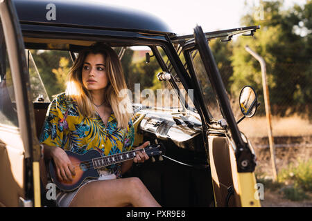 Jeune femme assise dans un van en jouant de la guitare Banque D'Images