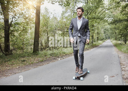 Businessman riding skateboard on rural road Banque D'Images