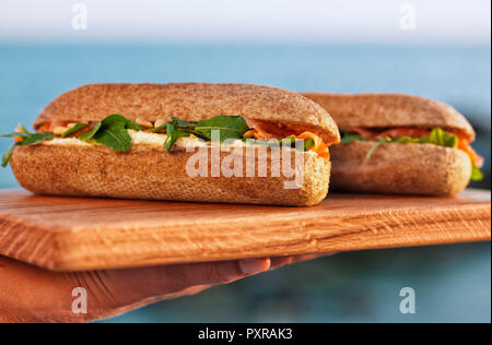 Woman's hand holding planche en bois avec deux sandwiches au saumon Banque D'Images