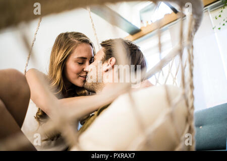 Affectueux heureux couple kissing in fauteuil suspendu à la maison Banque D'Images