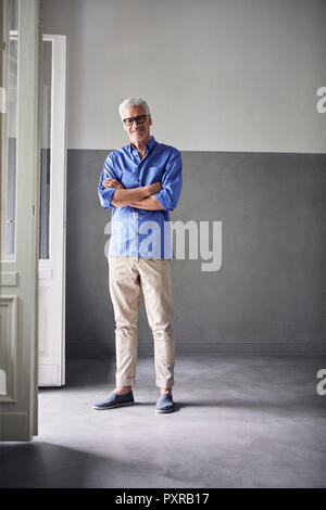 Portrait of smiling mature man debout à côté de la porte du balcon ouverte à la maison Banque D'Images