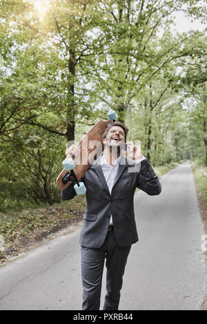 Happy businessman with skateboard parler sur smartphone on rural road Banque D'Images