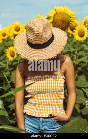 Méconnaissable femme avec un chapeau de paille dans un champ de tournesols Banque D'Images