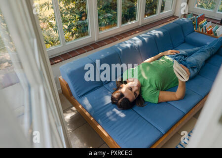 Young woman lying on couch at home reading book Banque D'Images