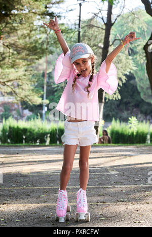 Happy little girl raising arms, tandis que le roller dans un parc Banque D'Images