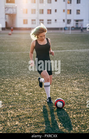 Jeune femme jouant au football sur le terrain de football de courir avec la balle Banque D'Images