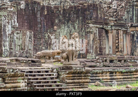 Unrestaured guardian statues d'un naga Cambodgien, garudas et un lion et des bas-reliefs de devatas dans le temple Bayon à Angkor Thom au Cambodge Banque D'Images