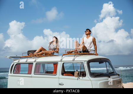 Jeune couple avec des lunettes de soleil assis sur le dessus de toit minifourgonnette Banque D'Images