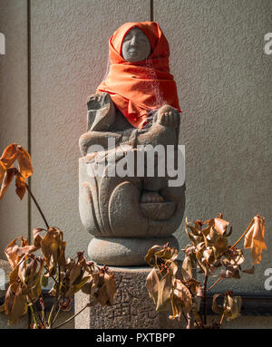 Statue sacrée, avec robe rouge et d'araignées, des offrandes de feuilles flétries, serein dans le soleil, Higashi, Kagawa, Japon Banque D'Images