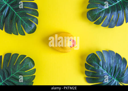 Mise à plat de canard en caoutchouc et feuilles de palmier tropical sur fond jaune. Un minimum d'été concept créatif. Banque D'Images