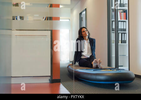 Businesswoman sitting on paddle board, daydreaming in office Banque D'Images