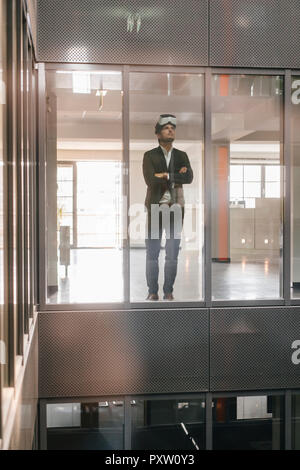 Businessman standing in office building, regardant à travers des lunettes VR