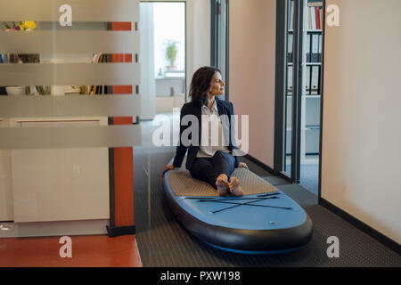 Businesswoman sitting on paddle board, daydreaming in office Banque D'Images