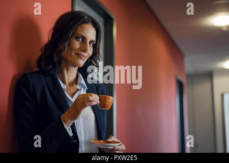 Young businesswoman standing in office corridor, boire du café Banque D'Images