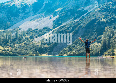 Autriche, Tyrol, randonneur au lac Seebensee debout dans l'eau jusqu'aux chevilles, avec les bras levés Banque D'Images