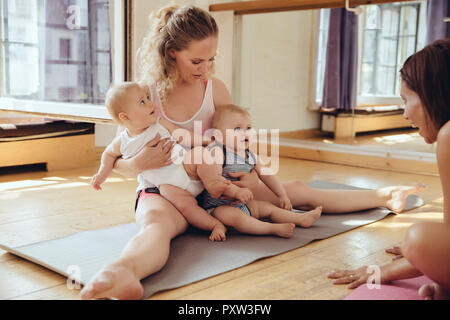 Mère avec des lits bébés assis sur un tapis de yoga Banque D'Images