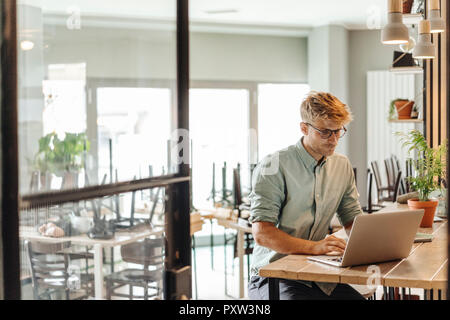 Jeune homme travaillant dans sa start-up cafe, using laptop Banque D'Images