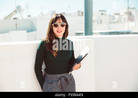Avec des lunettes de soleil femme debout sur toit, holding laptop Banque D'Images