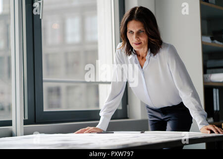 Businesswoman working in office, looking at blueprints Banque D'Images