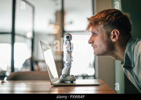 Man looking at toy robot, debout sur son ordinateur portable Banque D'Images