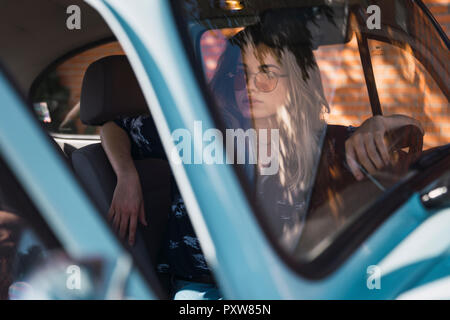 Jeune femme portant des lunettes de soleil assise dans une voiture Banque D'Images