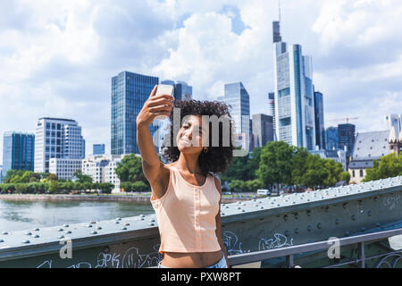 Allemagne, Francfort, portrait of content jeune femme avec des cheveux bouclés en tenant en face de selfies skyline Banque D'Images