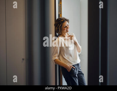 Businesswoman leaning détendu dans le cadre de la porte de son bureau Banque D'Images