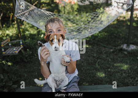 Garçon assis avec Jack Russel terrier sur son tour dans le jardin Banque D'Images