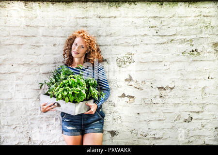 Portrait de jeune femme avec des herbes fraîches dans une boîte appuyé contre un mur de briques blanches Banque D'Images