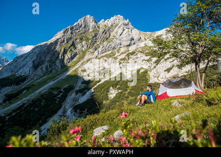 Autriche, Tyrol, randonneur prenant une pause, assis dans l'herbe par sa tente Banque D'Images