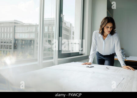 Businesswoman working in office, looking at blueprints Banque D'Images