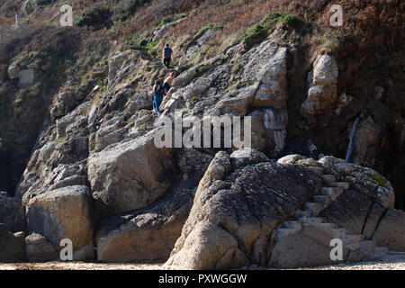 Plage de Porthcurno les visiteurs de l'escalade rocheuse et escarpée, Étapes vers le théâtre Minnack ci-dessus sur le chemin du littoral cornouaillais. Banque D'Images