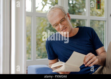 Smiling mature man at home reading book Banque D'Images