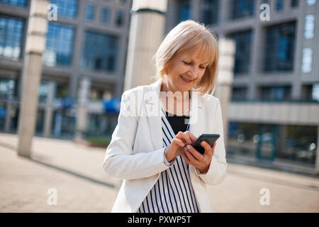 Outdoor portrait of happy senior businesswoman qui est l'utilisation de smartphone. Banque D'Images