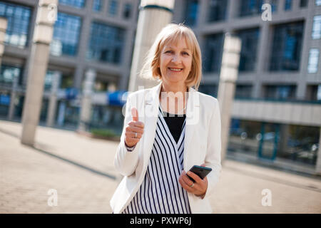 Outdoor portrait of happy senior businesswoman qui est l'utilisation de smartphone. Banque D'Images