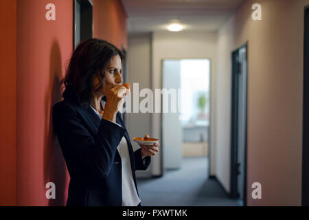 Young businesswoman standing in office corridor, boire du café Banque D'Images