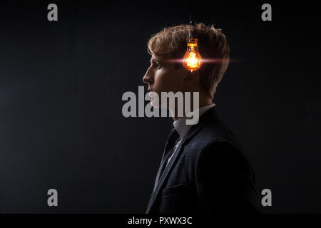 Profil d'un jeune homme avec une ampoule dans sa tête. Concept d'idée la naissance. Fond noir Banque D'Images