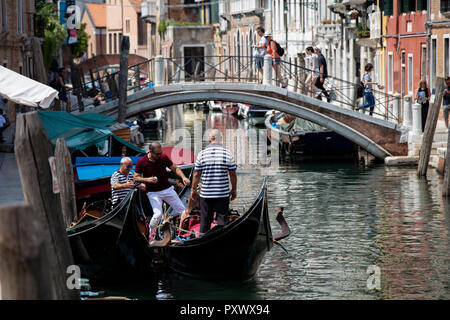 Un touriste d'être aidé dans une gondole par deux gondoliers sur un canal à Venise. Banque D'Images