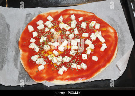 Une vue étroite de matières de la pizza, avec des dés de tomate, mozzarella et origan, avant d'être cuit dans un four, sur un plateau, typique de la cuisine italienne Banque D'Images